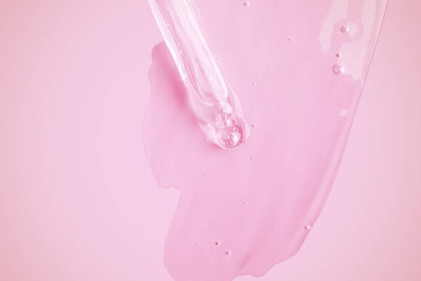 Een vloeiende heldere gel uit een pipet. Veel vloeiende gel op de achtergrond gesmeerd. Met bubbels. Op een roze achtergrond. - Foto, afbeelding