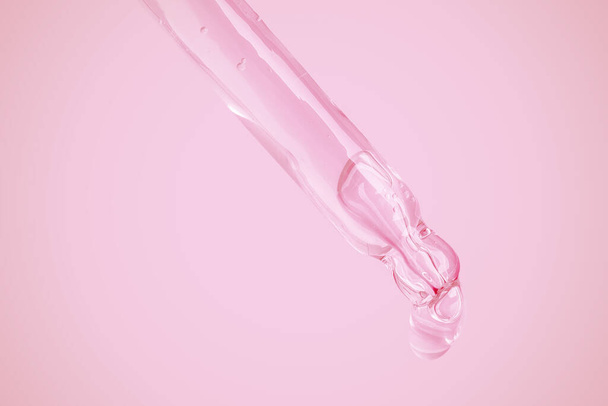 Transparante gel uit een oogdruppelaar lekken op een roze achtergrond. Bubbels van de gel. Geltextuur.  - Foto, afbeelding