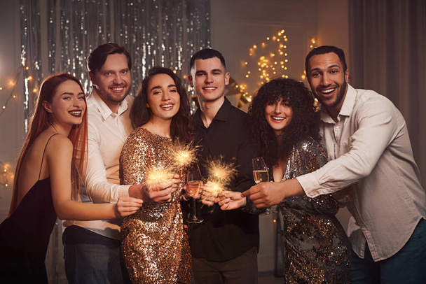 Happy friends with glasses of wine and sparklers celebrating birthday indoors - Foto, imagen