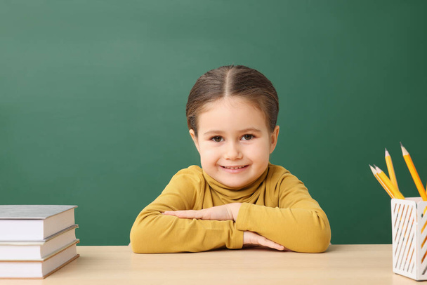 Happy little school child sitting at desk with books near chalkboard - Valokuva, kuva