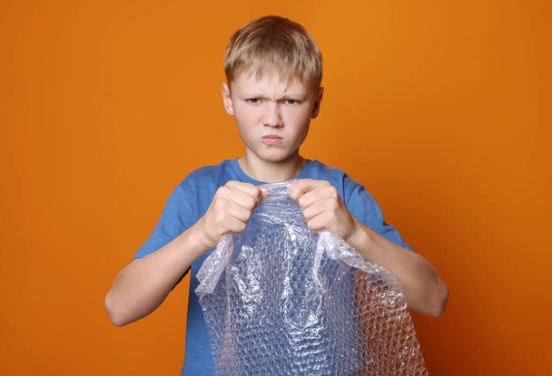 Angry boy popping bubble wrap on orange background. Stress relief - Zdjęcie, obraz