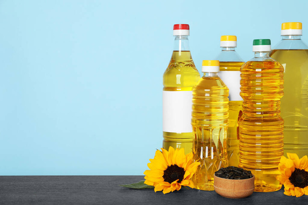 Bottles of cooking oil, sunflowers and seeds on wooden table, space for text - Fotoğraf, Görsel