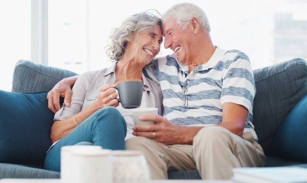 Ты все еще знаешь, как заставить меня улыбнуться. пожилая пара наслаждается расслабляющим кофе-брейком на диване дома - Фото, изображение