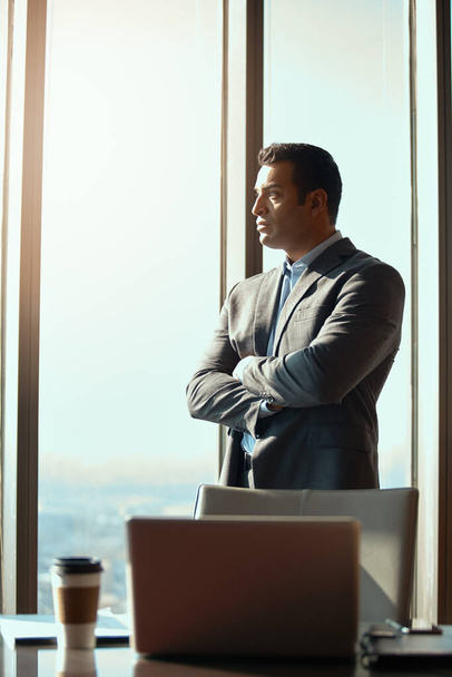 Confidence got him to the top. a handsome young businessman standing with his arms folded in the office - 写真・画像