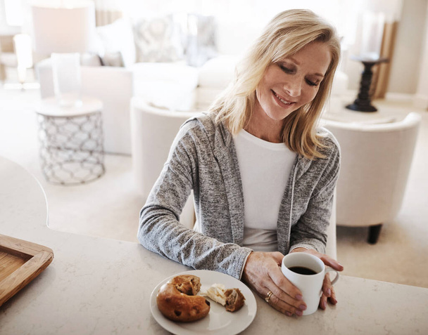 Все дело в этих простых удовольствиях. зрелая женщина пьет кофе и перекусывает в расслабленный день дома - Фото, изображение