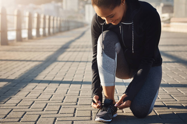 La forma fisica inizia con quel primo passo. una giovane donna in forma legandosi i lacci delle scarpe prima di andare a correre sul lungomare - Foto, immagini