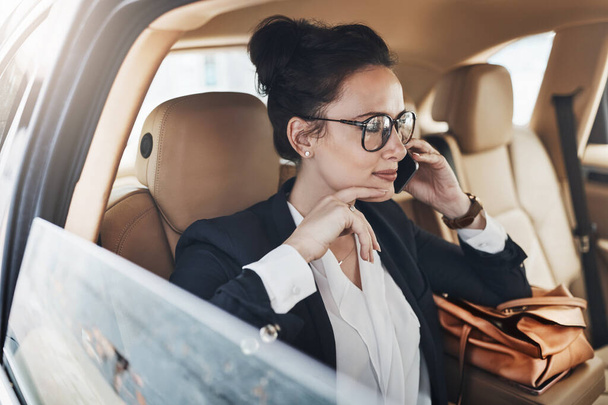 ¿Cuáles son nuestras fechas límite. una joven y confiada mujer de negocios sentada en un coche como pasajera y hablando por su celular mientras iba a trabajar - Foto, Imagen