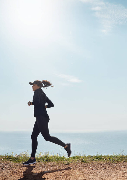 Raggiungerà il suo obiettivo. una giovane donna determinata che va a correre da sola con una vista sull'oceano sullo sfondo - Foto, immagini