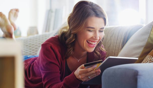 Una mujer feliz es una que puede comprar libremente en línea. una joven atractiva tumbada en su sofá y usando una tableta para ir de compras en línea - Foto, imagen