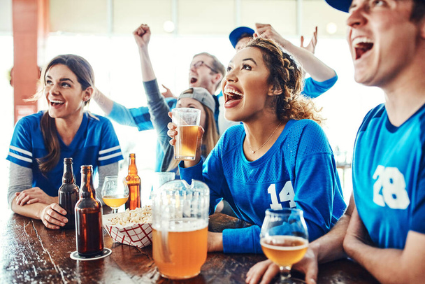 Enjoying the action while sipping on a good beer. a group of friends watching their favorite team live in a sports bar - 写真・画像