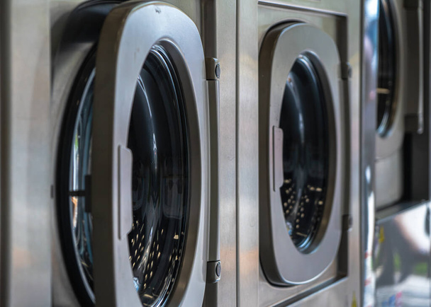 Máquinas de lavar roupa em uma lavanderia urbana para lavar e secar roupas, lençóis e toalhas de mesa em uma fileira com uma porta semi-fechada - Foto, Imagem