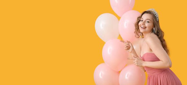 Beautiful young woman in prom dress and with balloons on yellow background with space for text - Фото, изображение