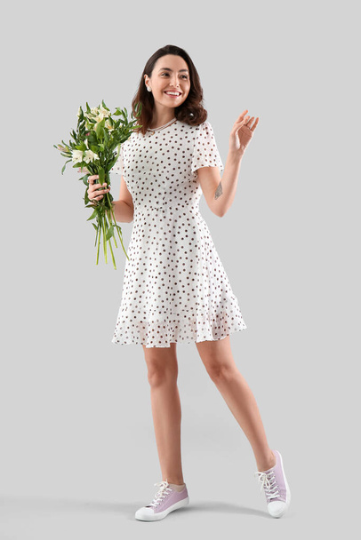 Young woman in dress with alstroemeria flowers on grey background - Foto, Imagen