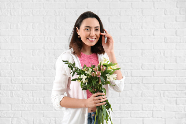 Young woman with alstroemeria flowers on white brick background - Foto, imagen