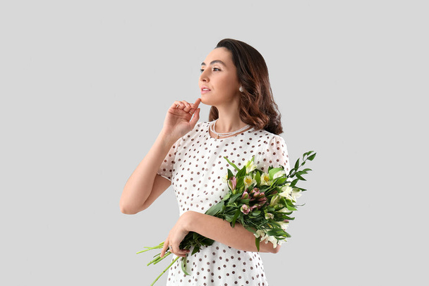 Jonge vrouw in jurk met alstroemeria bloemen op grijze achtergrond - Foto, afbeelding