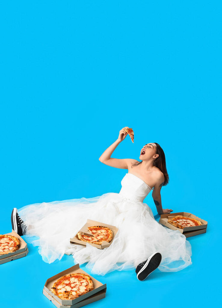 Mujer joven en vestido blanco con sabrosa pizza sentado sobre fondo azul - Foto, imagen