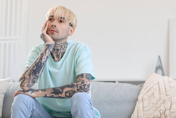 Young tattooed man sitting on sofa at home - Photo, Image
