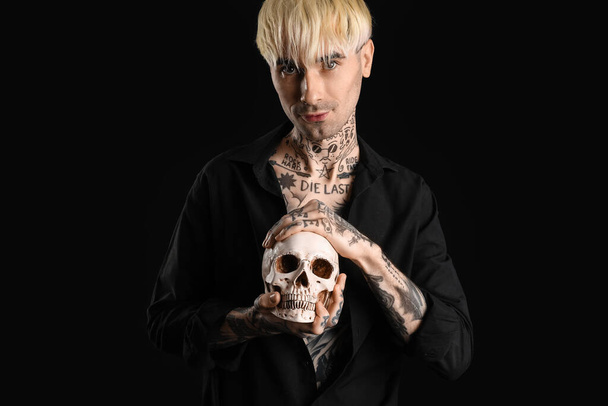 Tattooed young man with human skull on black background - Фото, изображение