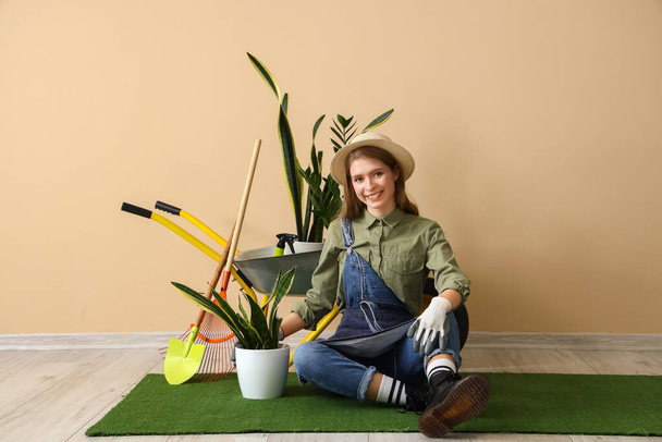 Jardinero femenino con plantas de interior y herramientas sentado cerca de la pared beige - Foto, Imagen