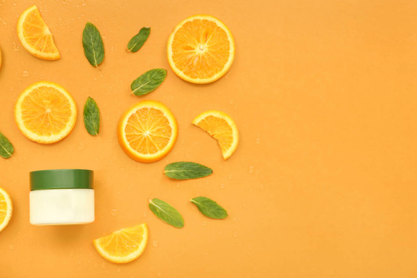 Jar of cosmetic cream with orange slices and mint on color background - Fotó, kép