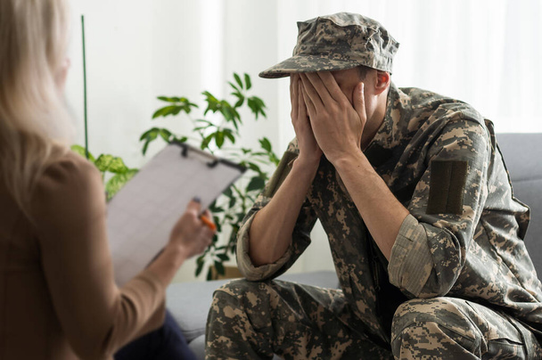 smutny żołnierz z ptsd mówi psychiatra i gestykulacji siedząc na kanapie podczas sesji terapii. - Zdjęcie, obraz