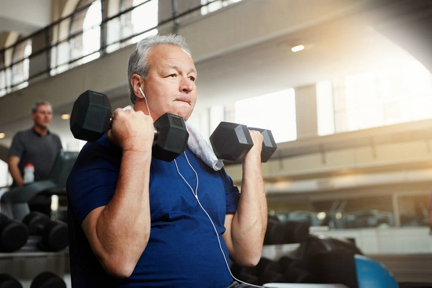 Nie sollte man seinem Alter vorwerfen, nicht fit zu sein. ein älterer Mann, der im Fitnessstudio mit Gewichten trainiert - Foto, Bild