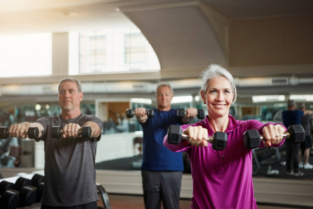 Az egyetlen szám, ami számít, hogy mennyit emelünk. egy idősebb csoport nő és a férfiak együtt edzenek súlyzókkal az edzőteremben. - Fotó, kép