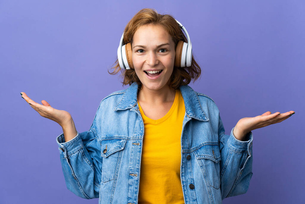 Junge Georgierin isoliert auf violettem Hintergrund überrascht und hört Musik - Foto, Bild