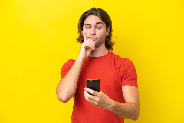 Kaukasischer gutaussehender Mann, isoliert auf gelbem Hintergrund, denkt und sendet eine Botschaft - Foto, Bild