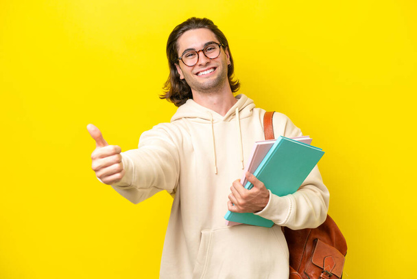 Νεαρός μαθητής όμορφος άντρας απομονωμένος σε κίτρινο φόντο κάνοντας μια χειρονομία - Φωτογραφία, εικόνα