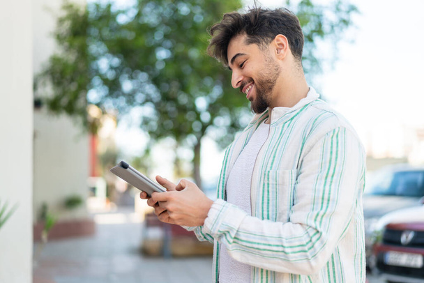 Hombre árabe guapo al aire libre sosteniendo una tableta con expresión feliz - Foto, Imagen