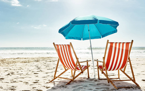 Get some summer in your life. Still life shot of two deck chairs under an umbrella on the beach - Foto, Imagen