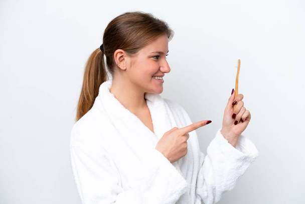 Mujer joven caucásica cepillándose los dientes aislados sobre fondo blanco apuntando hacia un lado para presentar un producto - Foto, Imagen