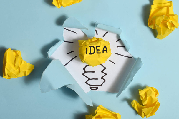 A piece of paper that says idea is in a hole with a yellow bulb. - Foto, Imagen