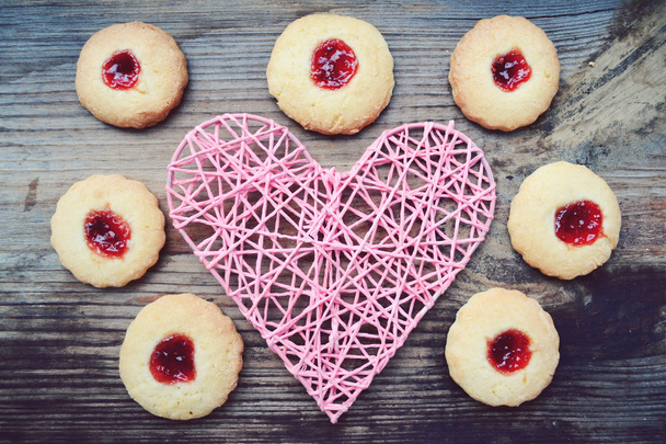 Concepto romántico con corazón rosa hecho a mano y un montón de galletas caseras con mermelada en la mesa de madera
 - Foto, imagen