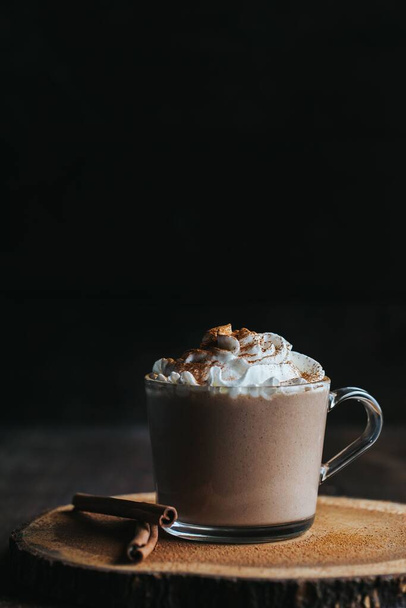 A vertical closeup shot of a glass of hot chocolate on a wooden board, with cream on top - Valokuva, kuva