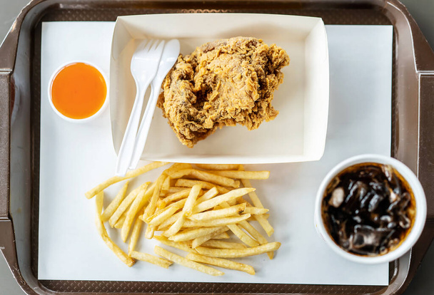 Top view of crispy fried chicken, french fries, chili sauce and soft drink on the side,  in the tray, photographed overhead with natural light - Fotó, kép