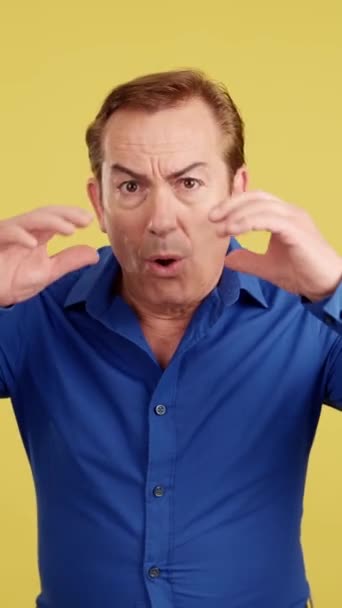 Surprised mature man gesturing that that he make a mistake in studio with yellow background - Séquence, vidéo