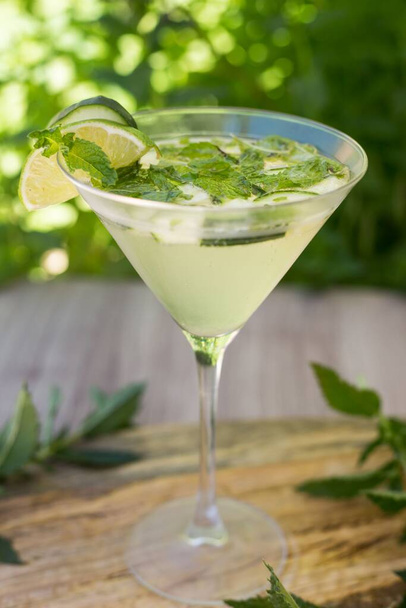 A vertical closeup shot of the glass of cocktail Margarita with mint and lime decorated with mint leaves on a wooden table - Foto, immagini