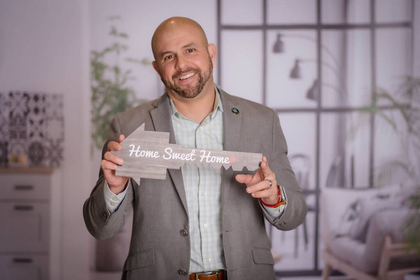 A closeup view of a man holding a wooden welcome board with a writing "Home sweet home" - Foto, Imagem