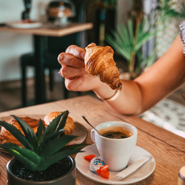 The view of a woman's hand holding the croissant over a cup of double espresso - Foto, Imagem