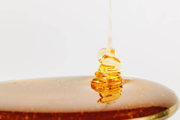 A close up shot of honey being poured into a silver spoon isolated on a white background - Fotó, kép