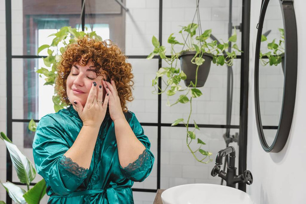 A chubby female with curly ginger hair applying makeup in a bathroom - Foto, afbeelding