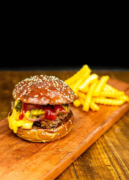 A vertical shot of burger sandwich with fries on wood isolated on black background - Foto, Bild