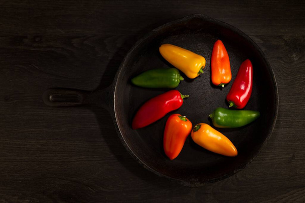 A top shot of four colorful peppers isolated on a black pan in a circle - Foto, afbeelding