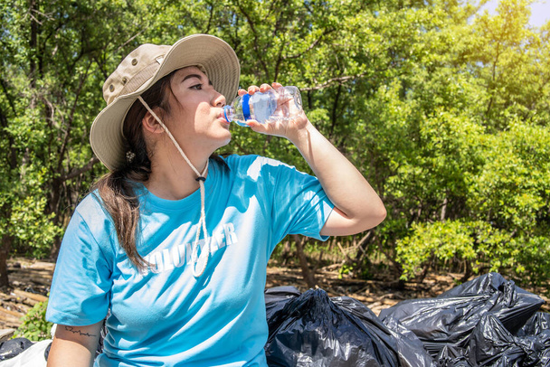 vrouwelijke vrijwilligers rusten en drinken water Na het helpen van de samenleving door het verzamelen van afval in het bos - Foto, afbeelding
