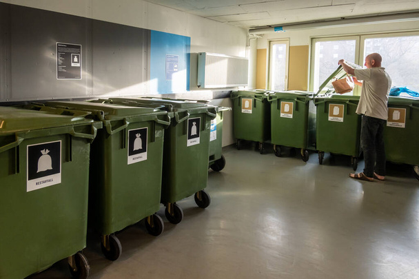 Estocolmo, Suecia Un hombre arroja basura en una sala de basura súper limpia y organizada en un complejo de viviendas residenciales.Las etiquetas denotan el tipo de residuos en sueco. - Foto, Imagen