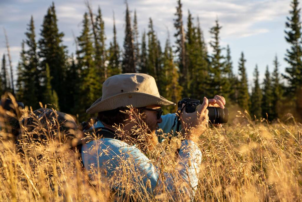 A male photographer taking shots lying on the grass with pine trees in the background - Photo, Image