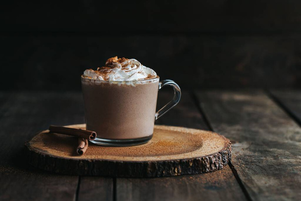 A closeup shot of a glass of hot chocolate on a wooden board, with cream on top - Fotó, kép