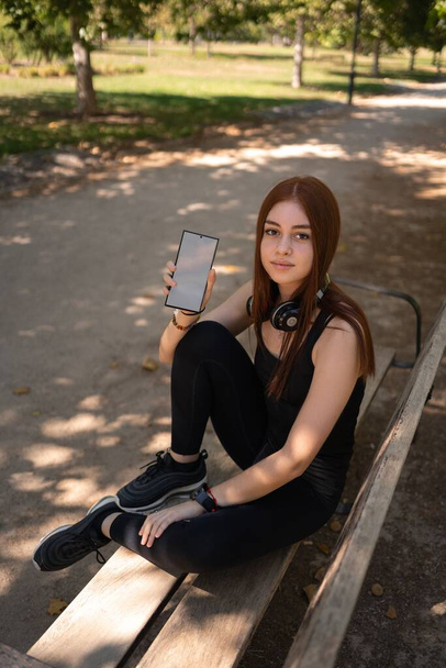 A girl sitting on a bench and demonstrating a mobile phone with a blank screen - Фото, зображення